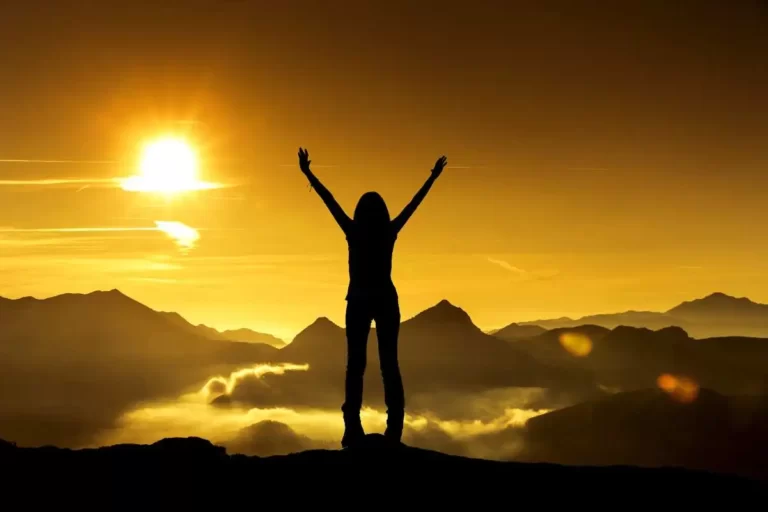 kobieta stojąca na szczycie z uniesionymi rękoma w górze, symbolizująca mentalność twórcy i sukces
